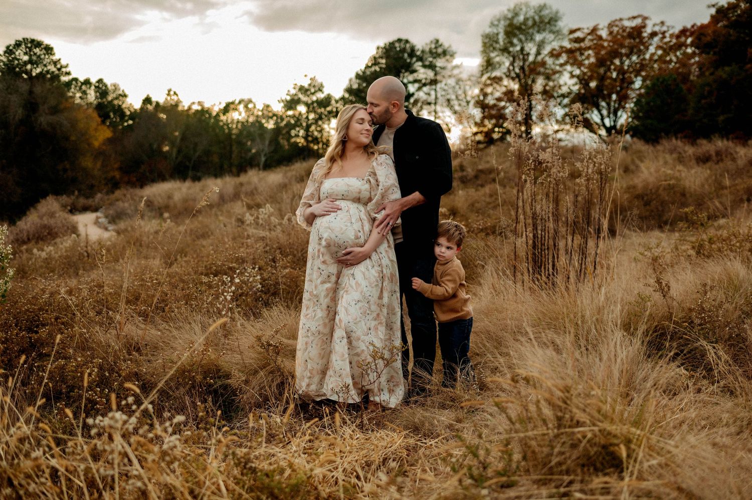 A couple embraces in a golden autumn field at sunset during intimate maternity photography session in Raleigh NC