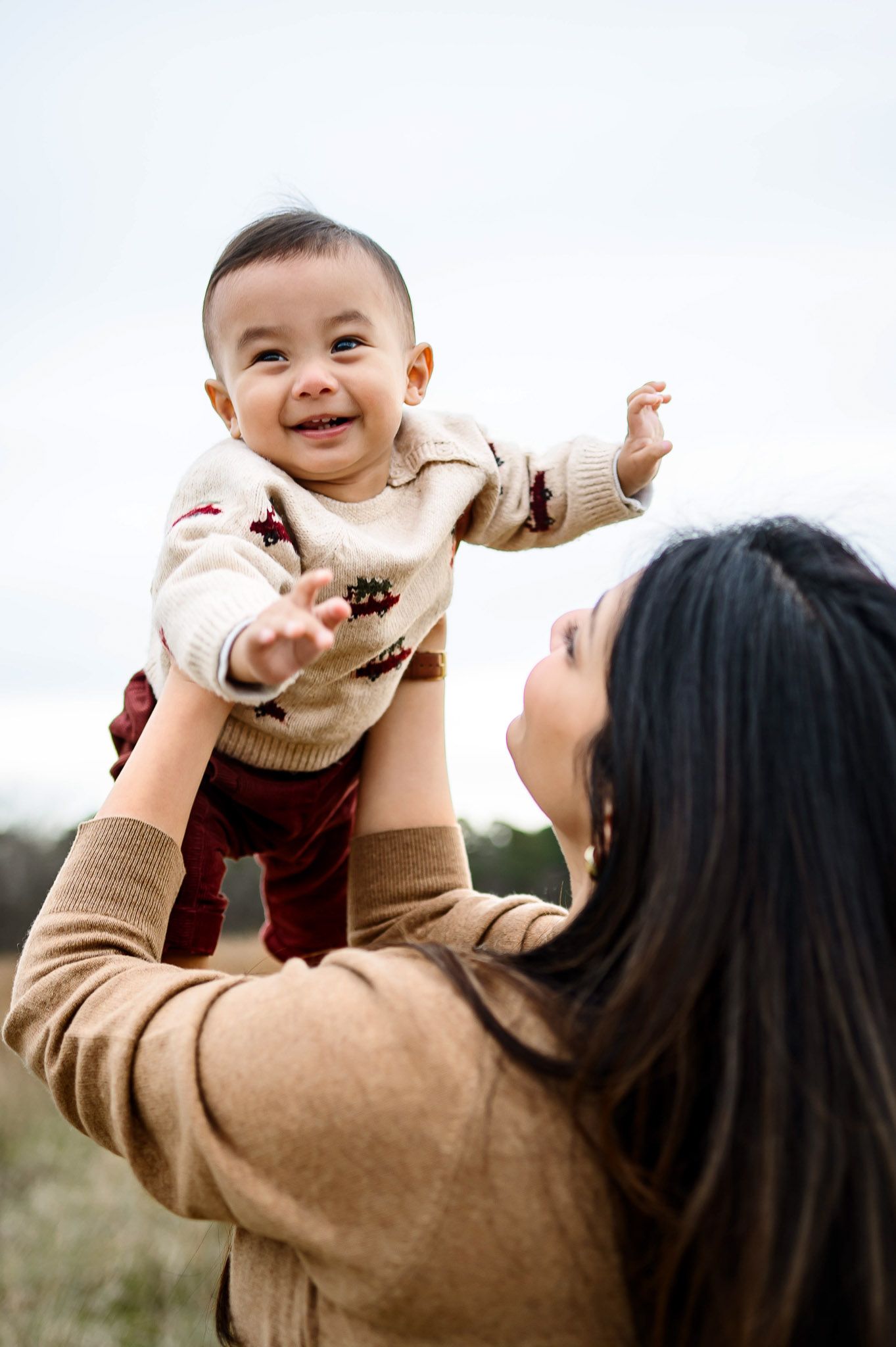 Mother lifting her smiling baby into the air during a natural outdoor family photography session in Durham NC