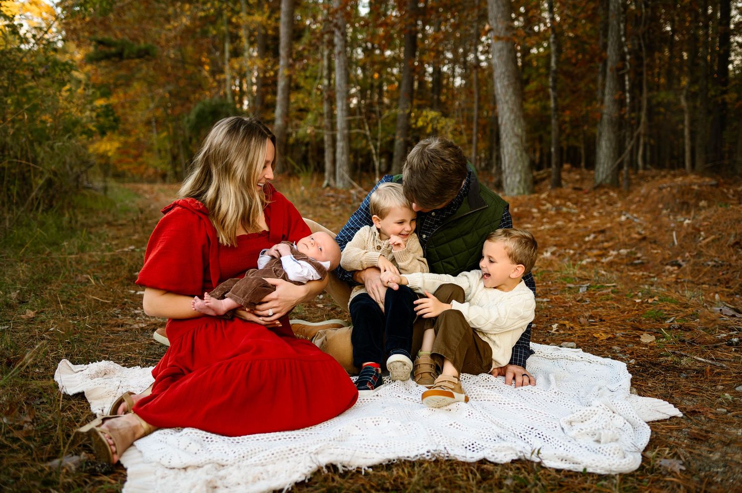 Raleigh family photographer captures parents with newborn and young children sitting together during a fall outdoor photo session