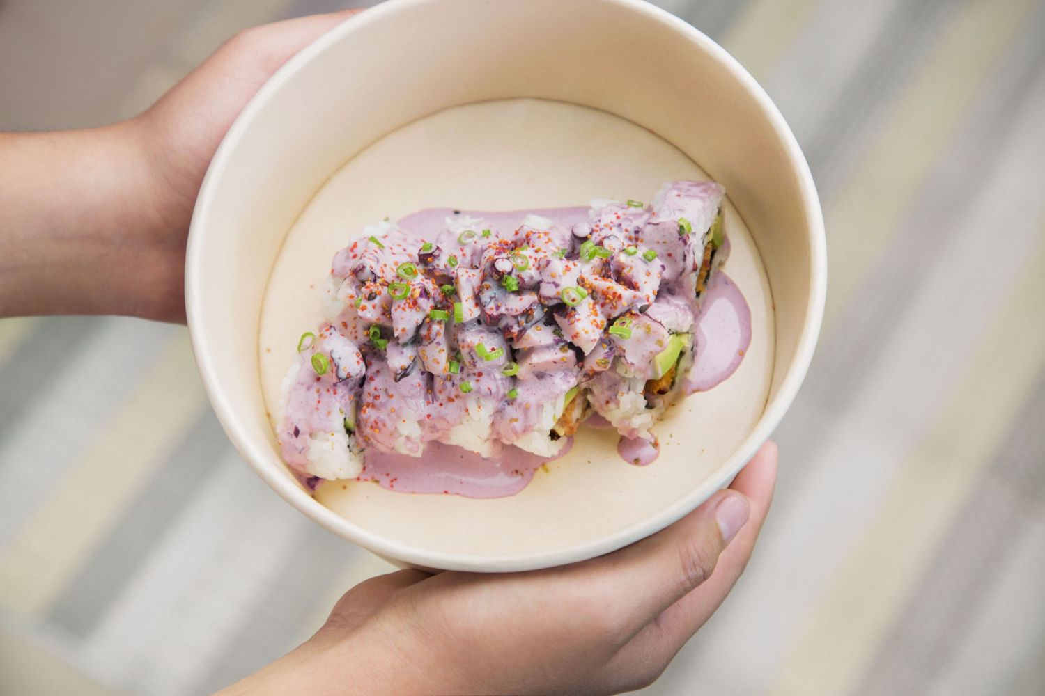 Hands hold a white bowl containing Pulpo al Olivo maki