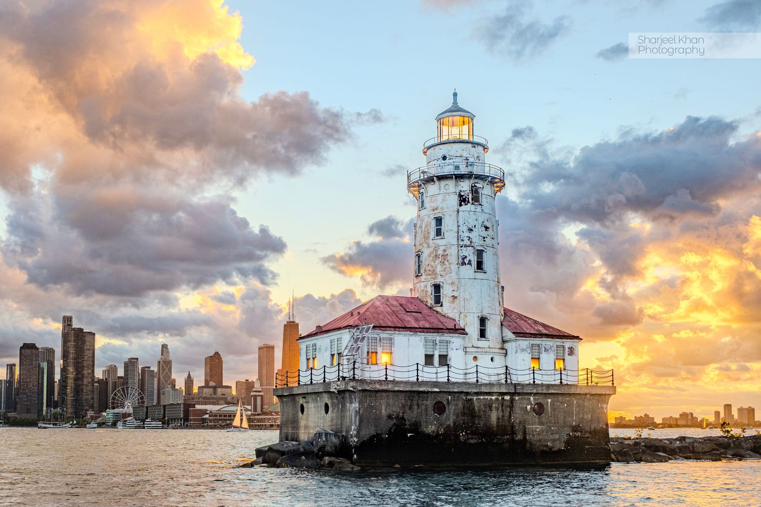 Lighthouse glowing at sunset against dramatic sky with Chicago skyline in background.