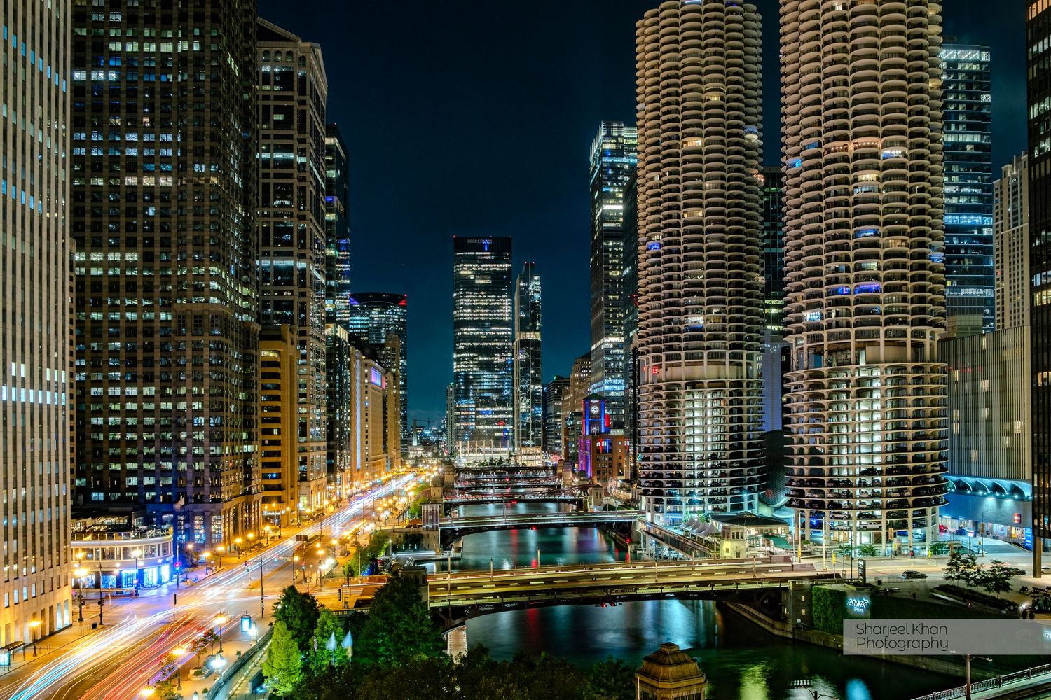 Illuminated cityscape of Chicago downtown at night with bridges spanning the river and tall skyscrapers.