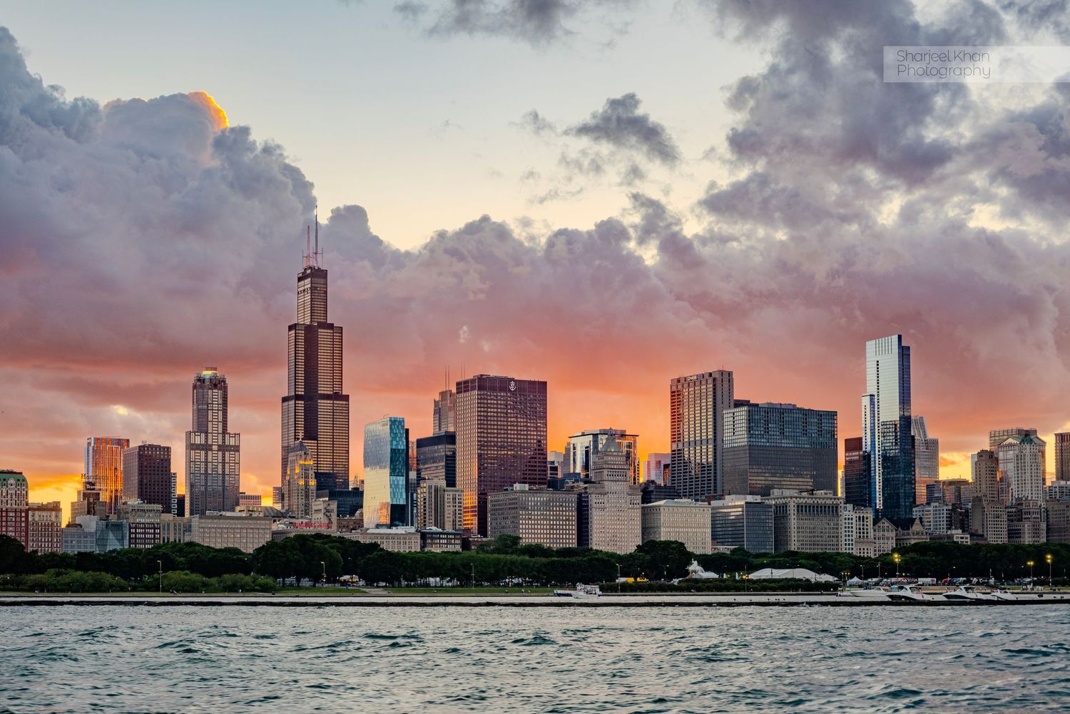Chicago skyline silhouetted against vibrant sunset sky reflecting in Lake Michigan.