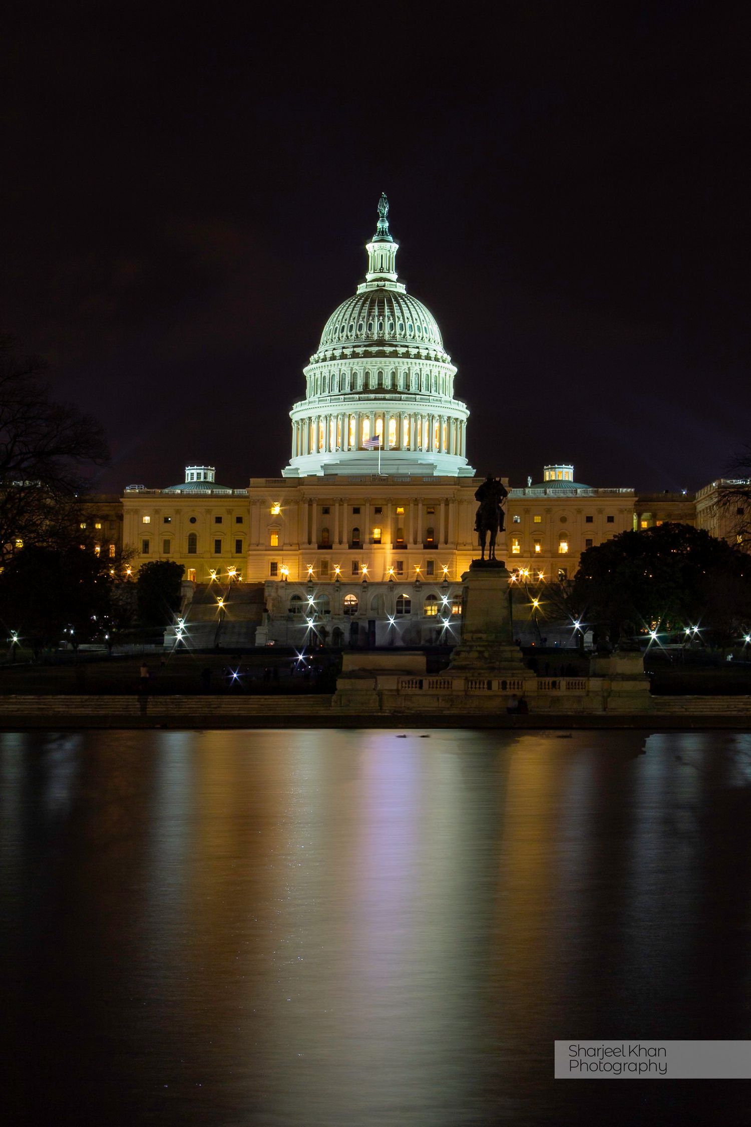 US Capitol building illuminated at night with reflection in water.