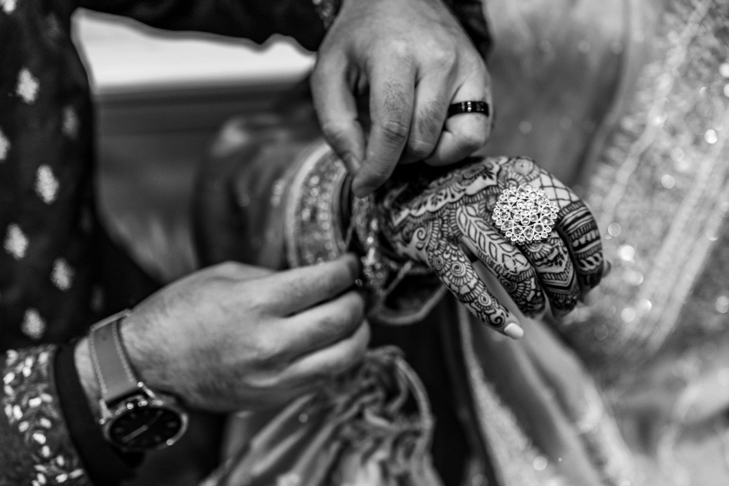 Black and white photo of hands working with intricate henna designs and jewelry.