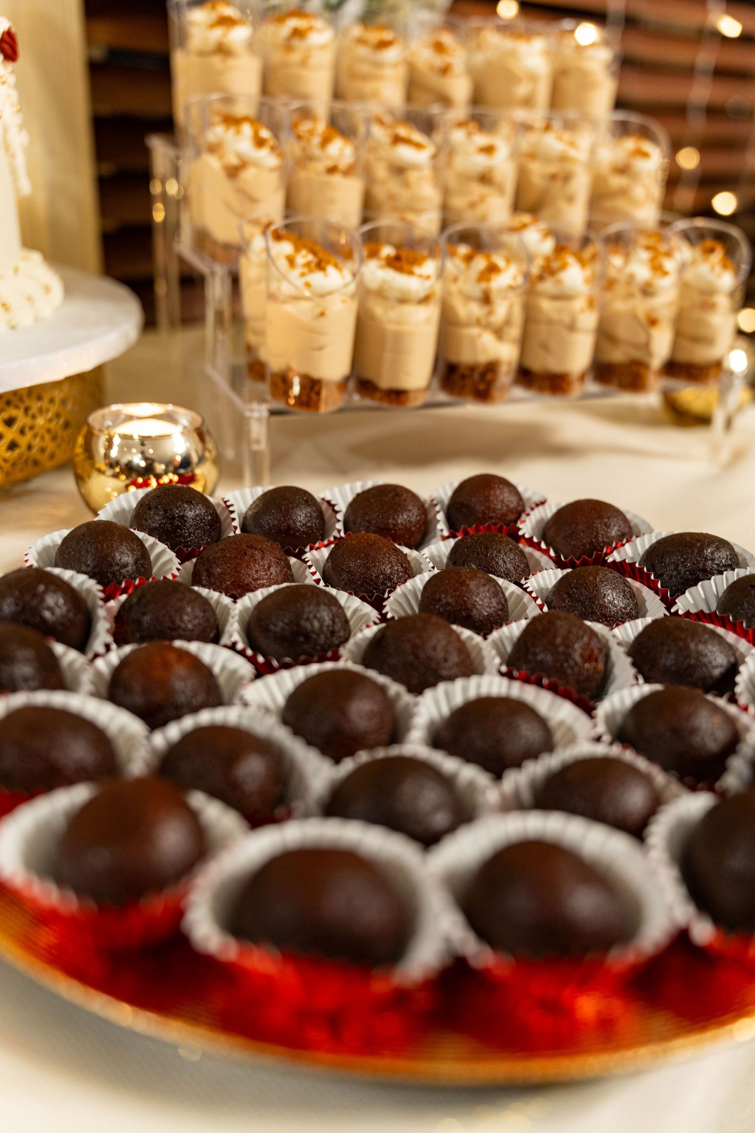A dessert table displays chocolate truffles on a red platter alongside small parfait glasses filled with layered treats.