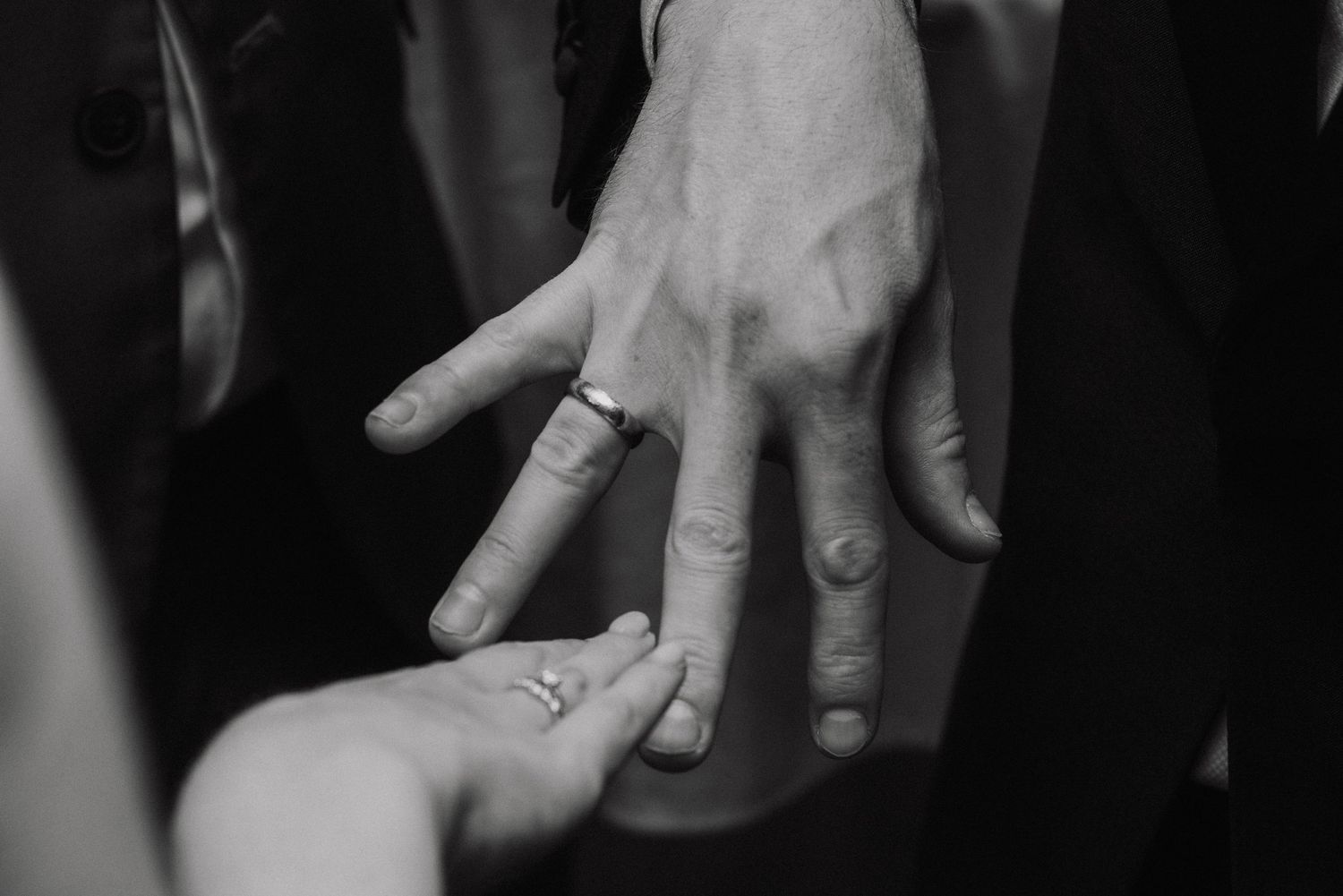 Black and white detail shot of hands exchanging wedding rings during ceremony.