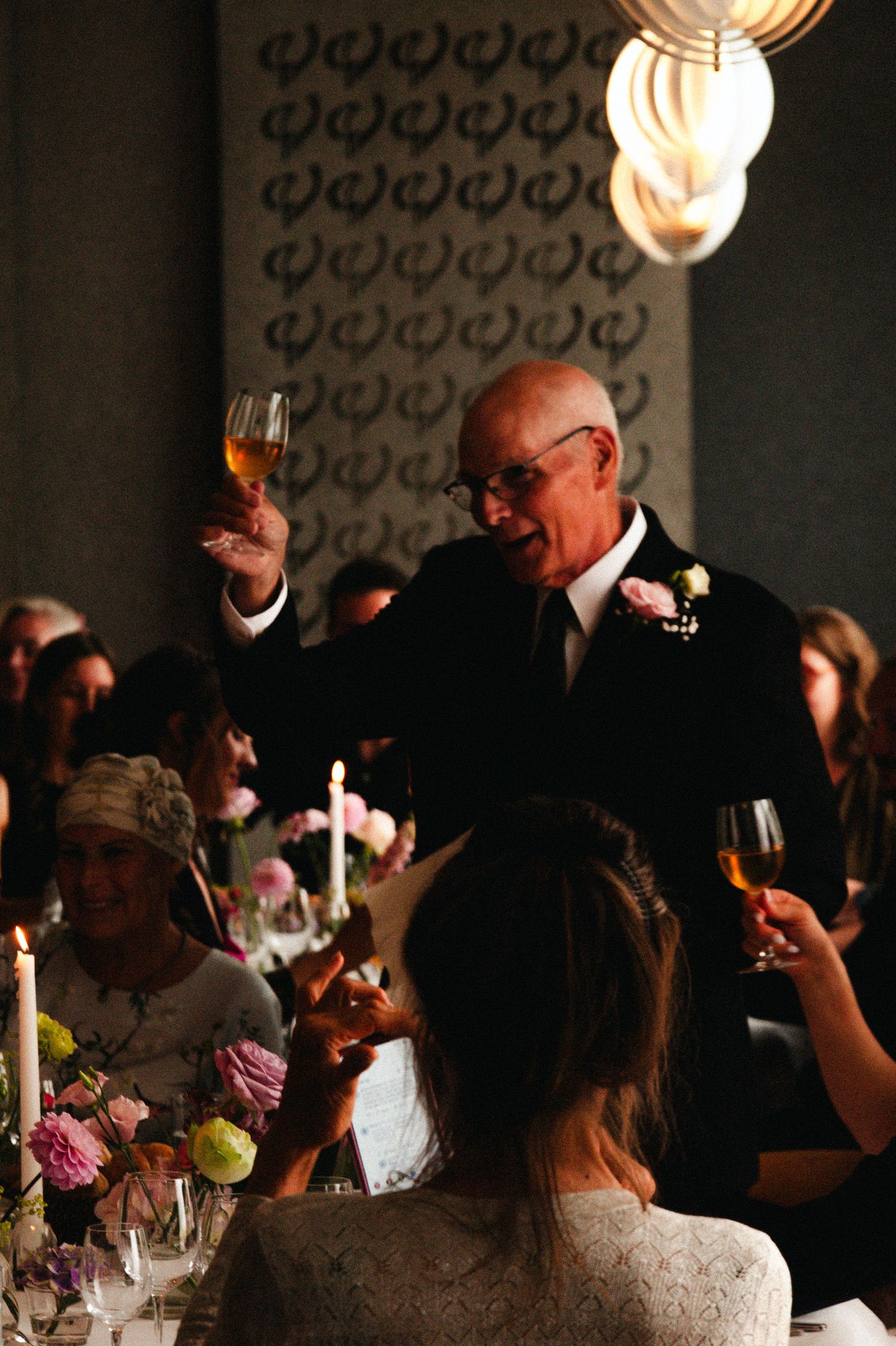 Wedding reception guests seated at a candlelit table with decorative lighting and floral centerpieces.