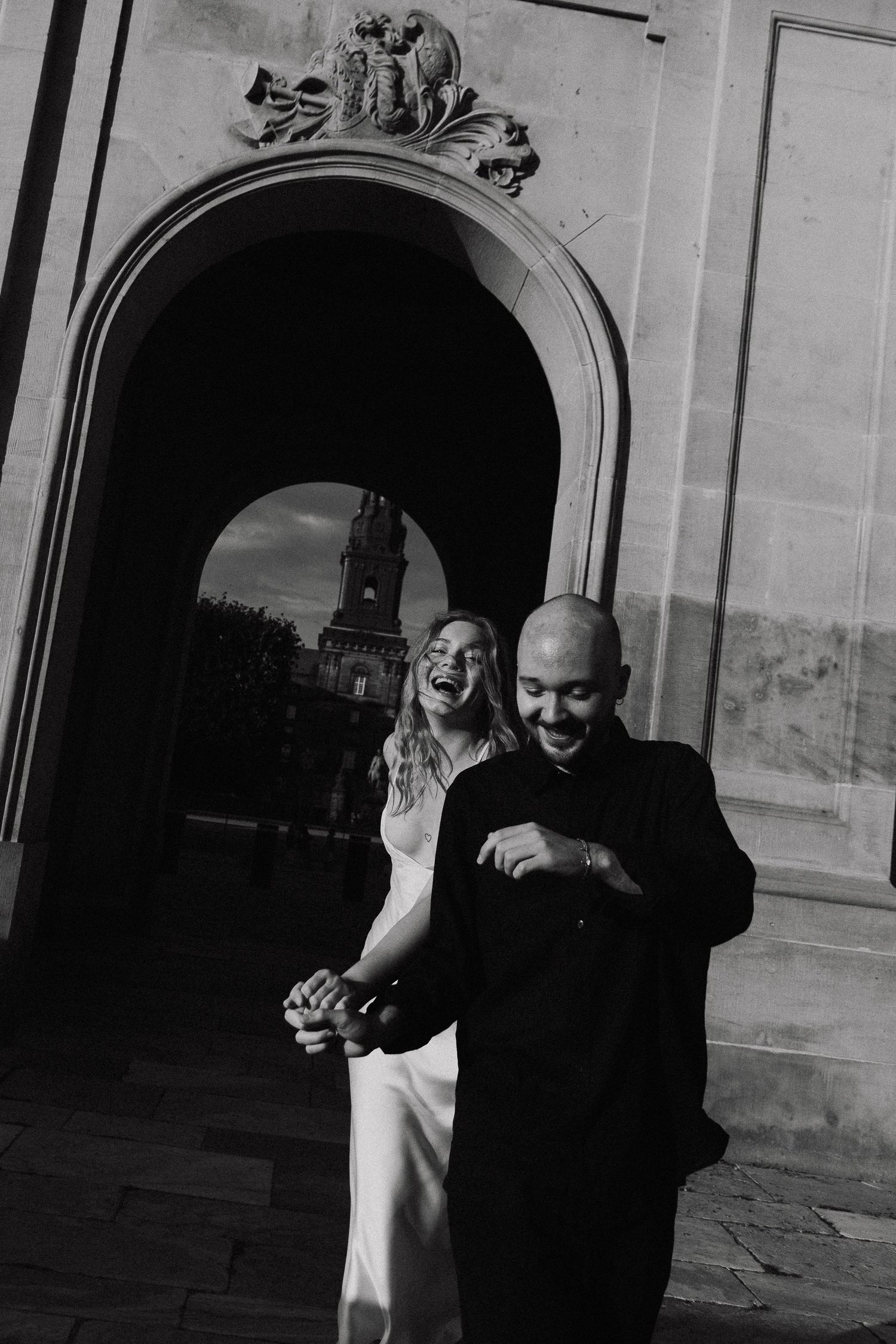 Black and white photograph showing a couple embracing and dancing in an elegant archway setting.