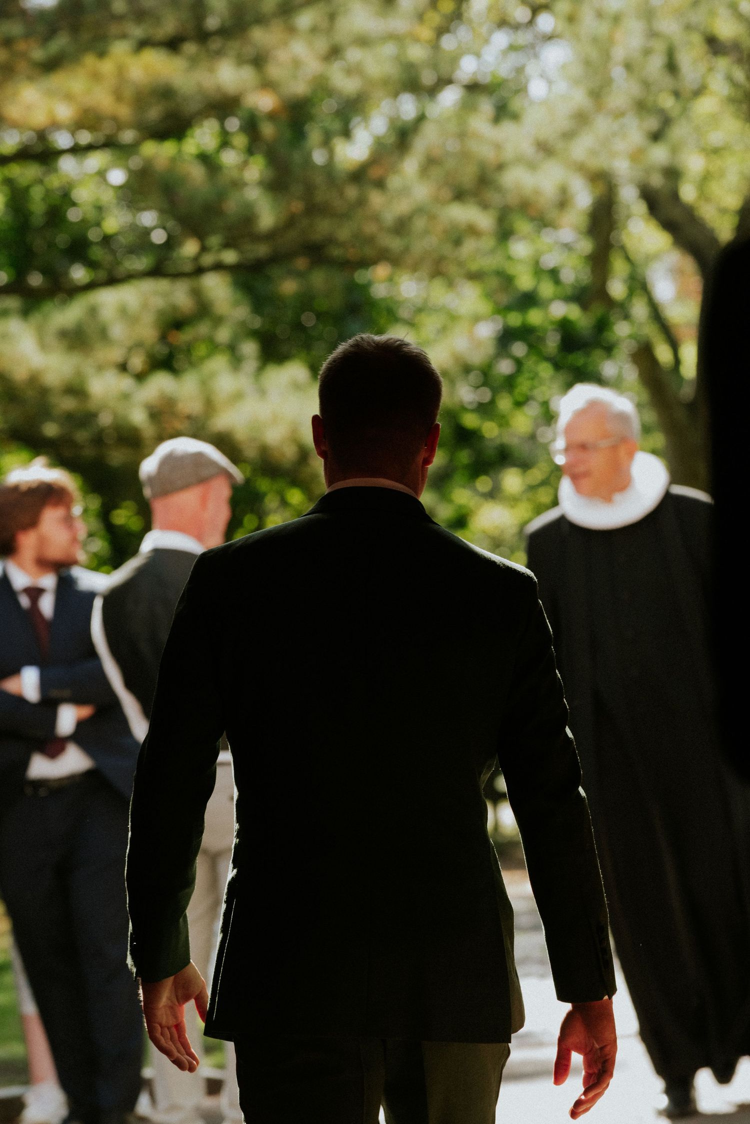 Groomsmen in black suits walk together outdoors during a wedding ceremony.