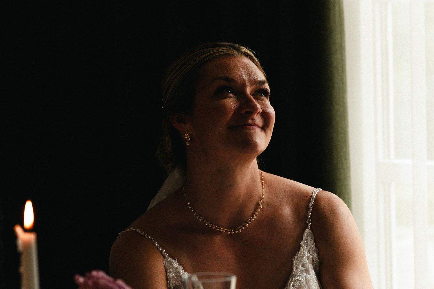 A bride in a white dress laughs joyfully while looking upward during a wedding celebration.