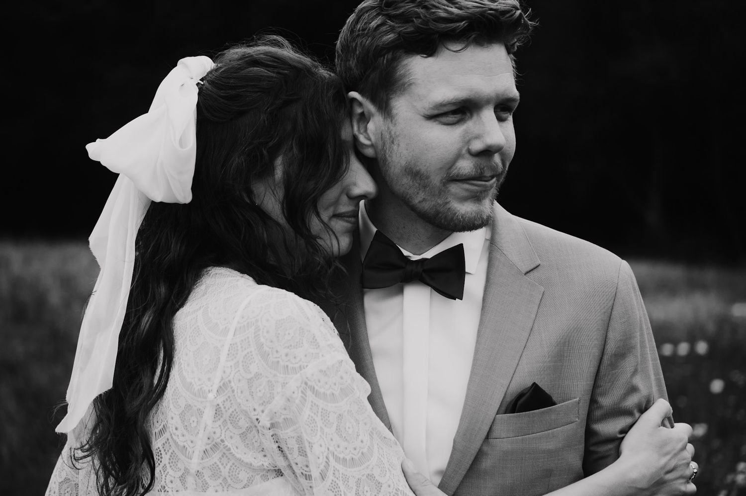 Black and white portrait of newlyweds in formal attire sharing an intimate moment outdoors.
