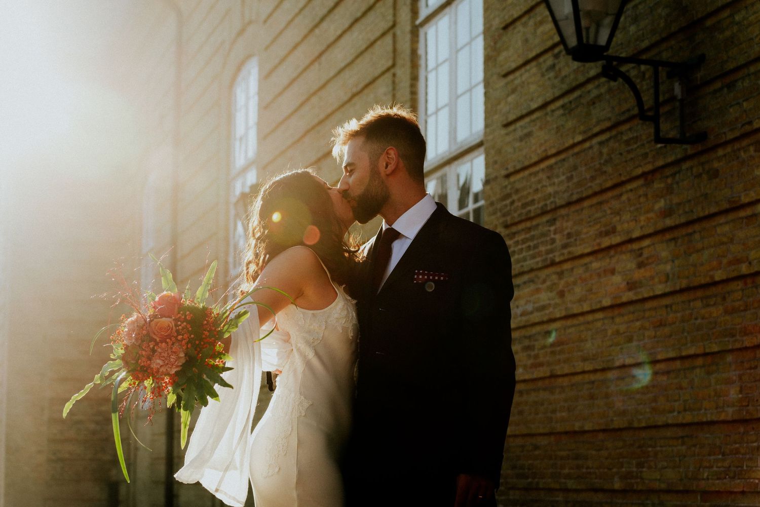 A romantic couple in formal wedding attire share a tender moment in a rustic barn setting with natural light streaming in.