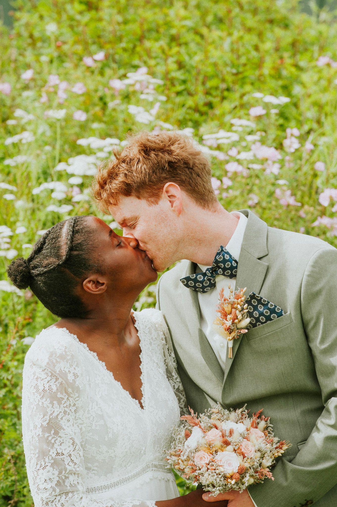 Wedding couple shares intimate moment among blooming wildflowers in summer field.
