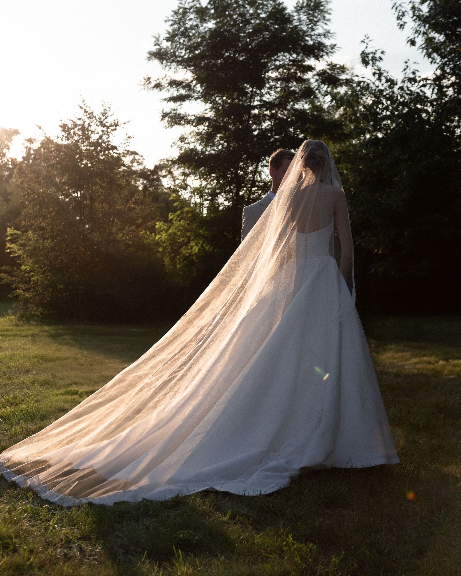 A flowing white wedding dress photographed in a dreamy outdoor setting during golden hour.