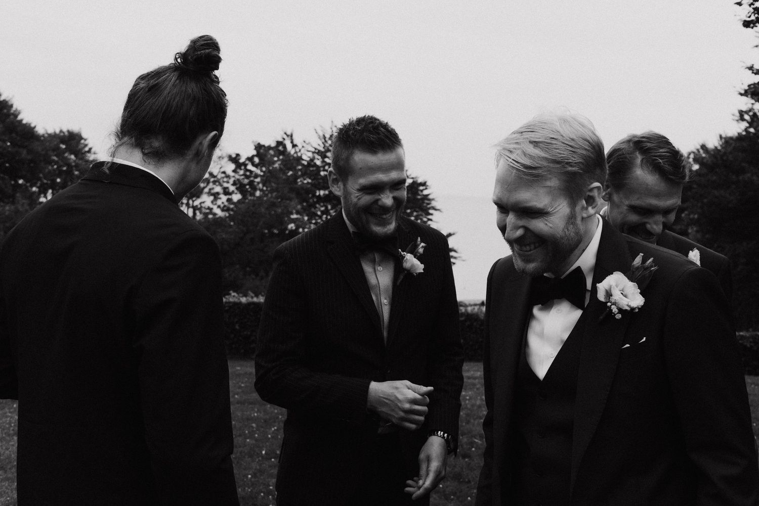 Wedding party members in formal attire gather outdoors for candid group photos at dusk.