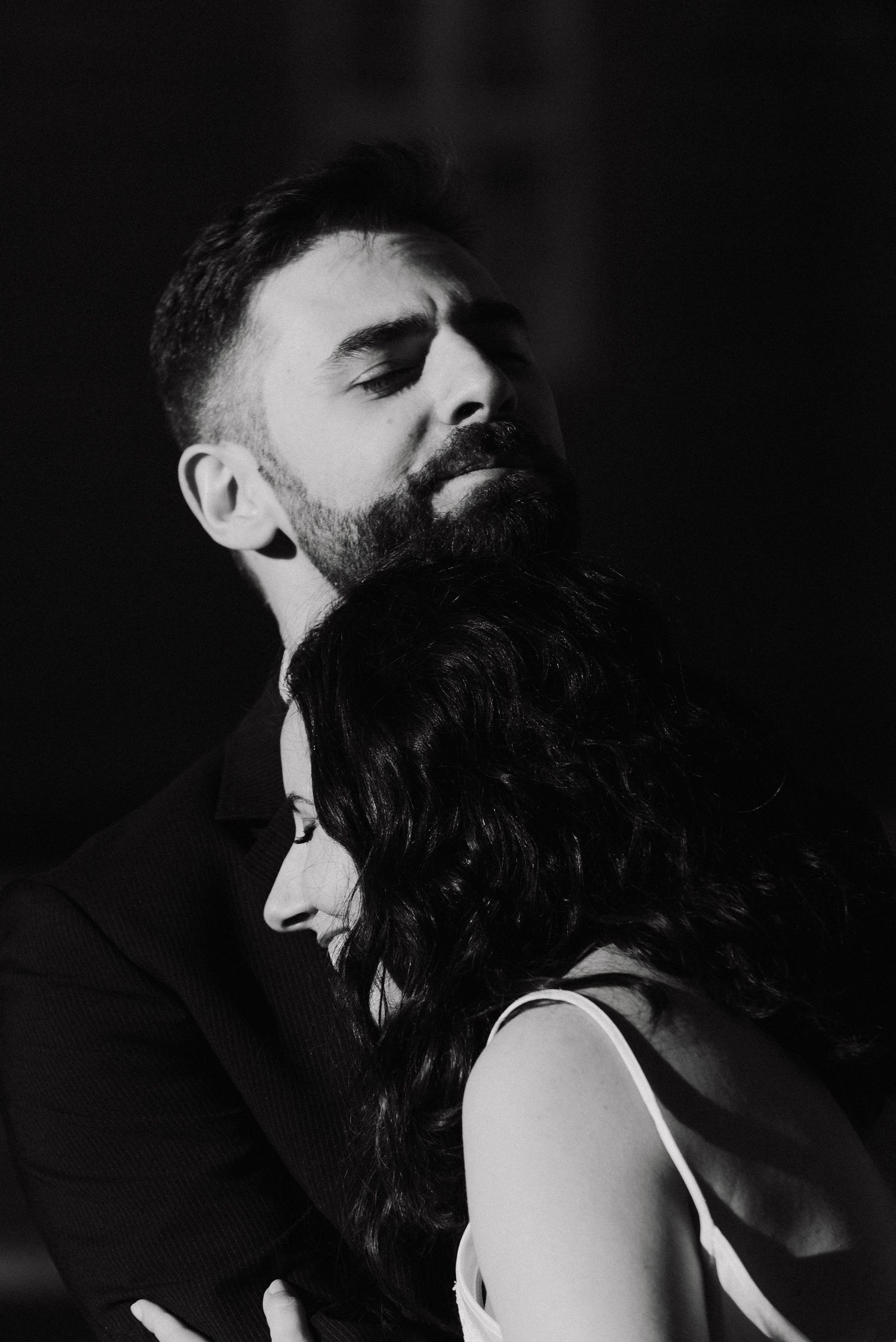 Intimate black and white portrait showing dramatic shadows and close physical connection.