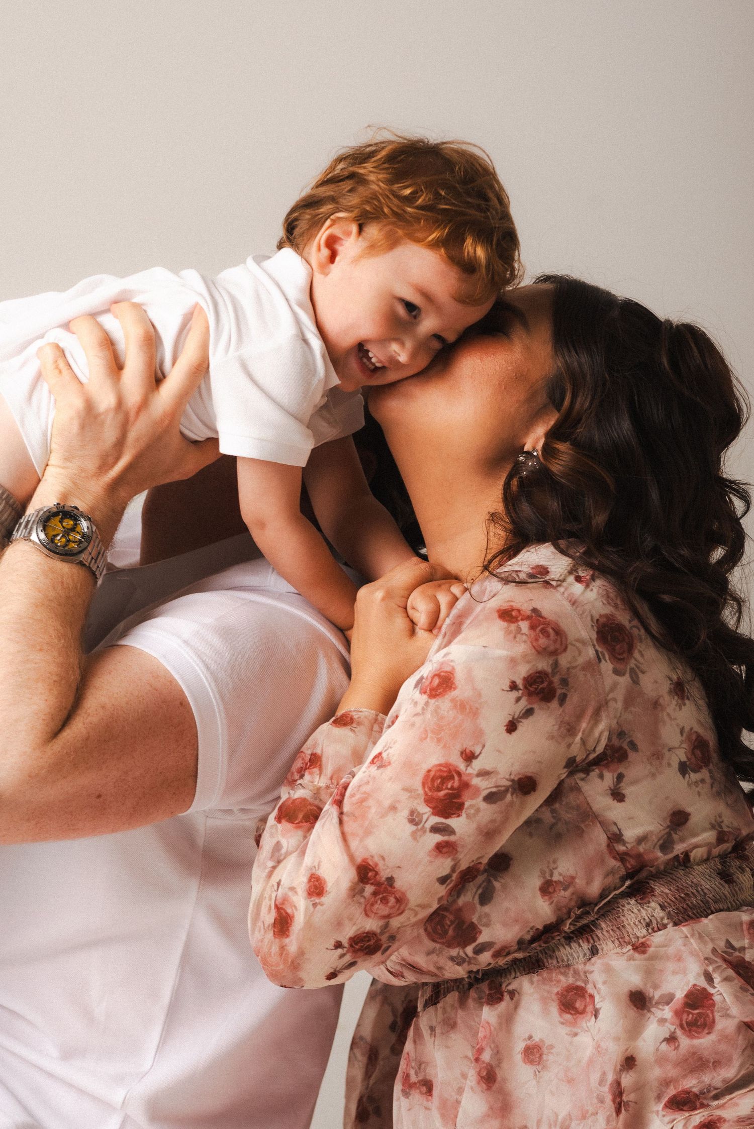 Romantic couple in white and floral dress share playful embraces in a minimalist studio setting.