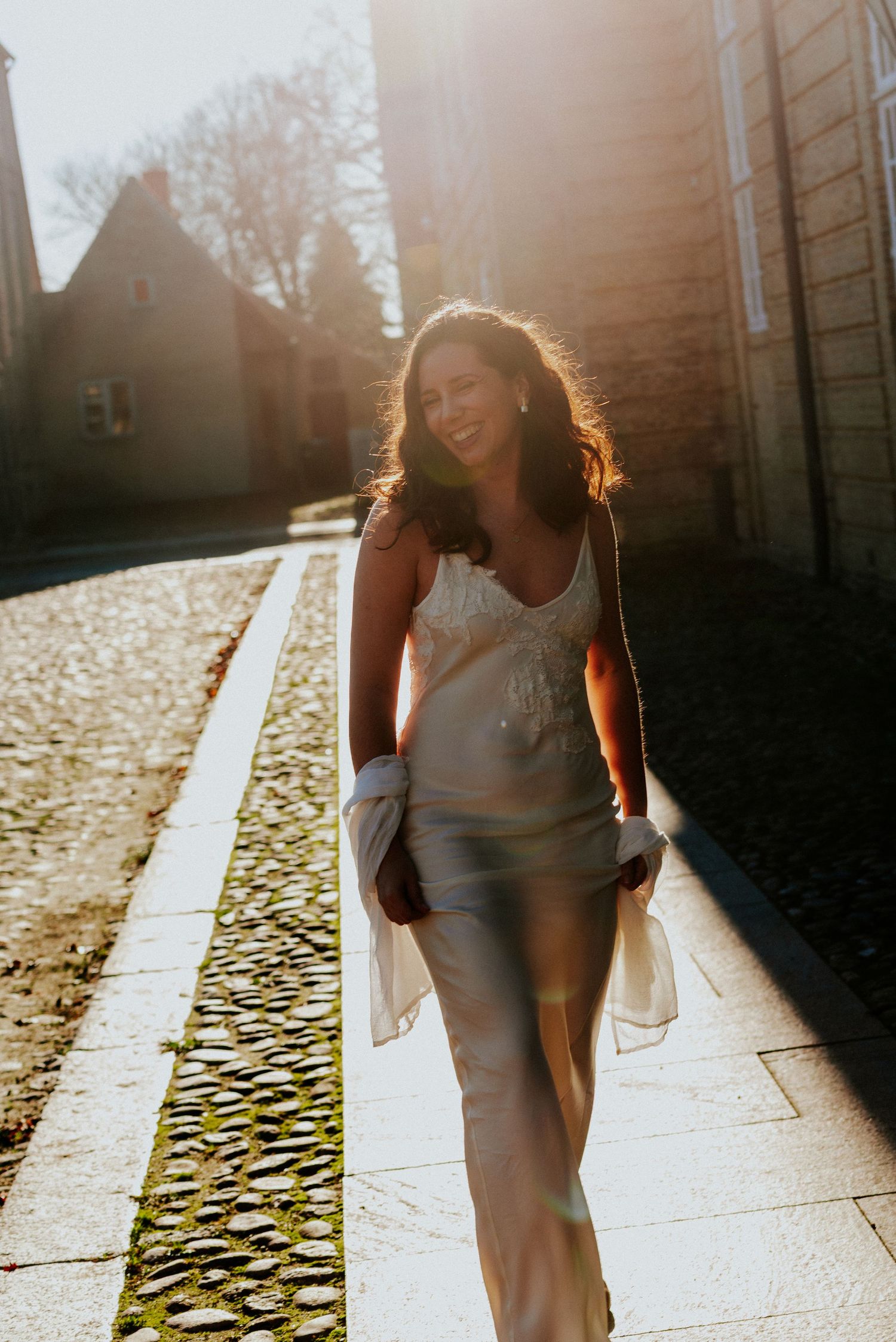 Couple walking together at sunset with dramatic backlighting and shadows on cobblestone path.