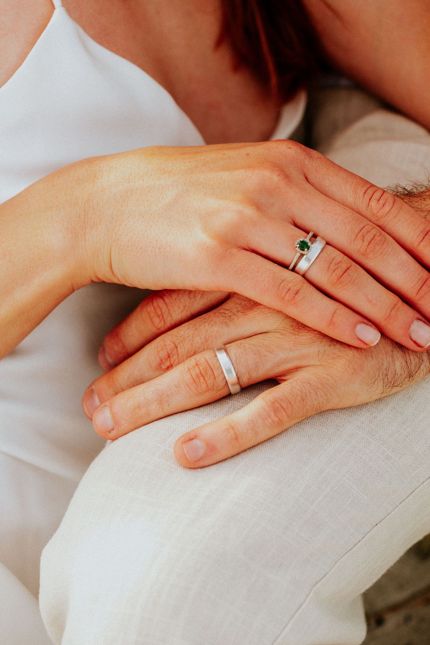 Close-up of hands wearing matching silver wedding bands resting on white fabric.