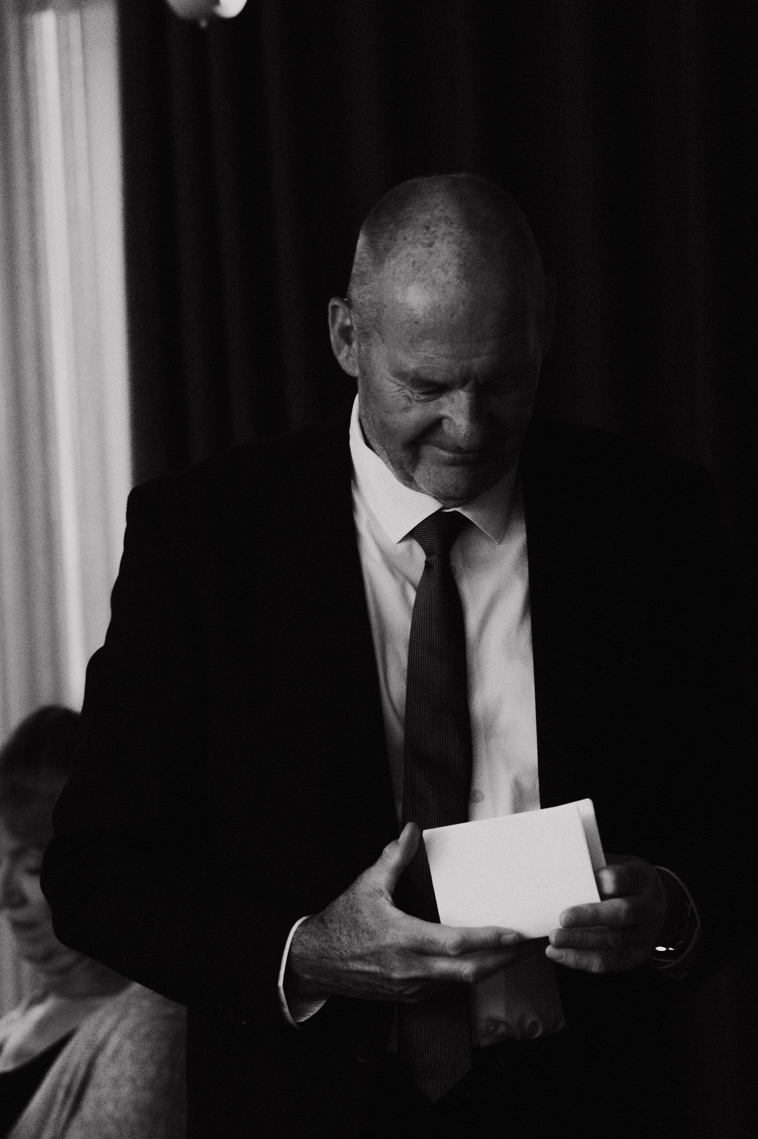 Black and white image of a person in a suit reading a letter in dramatic lighting.