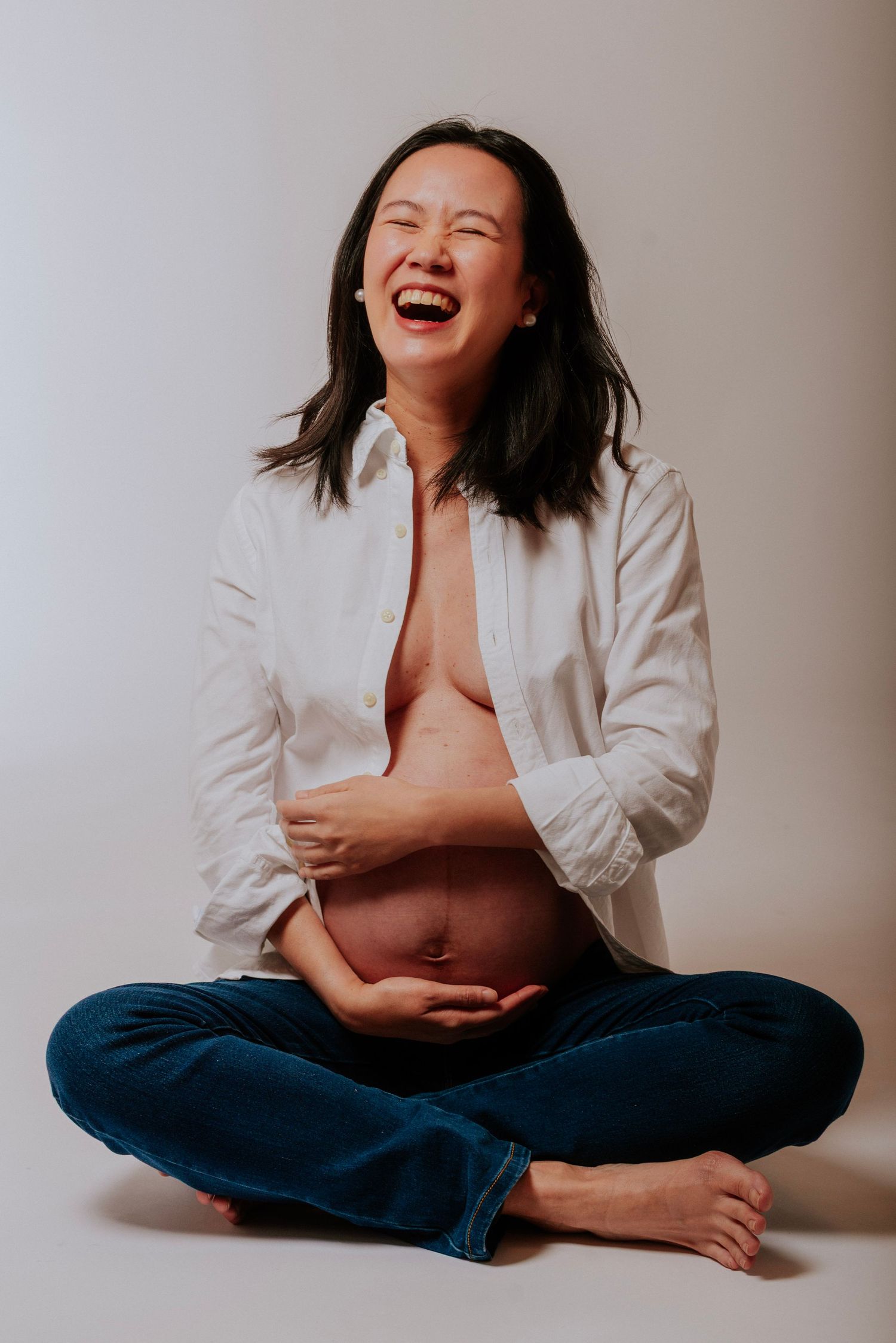 A person wearing a white shirt and jeans sits cross-legged on the floor in a series of candid laughing poses.