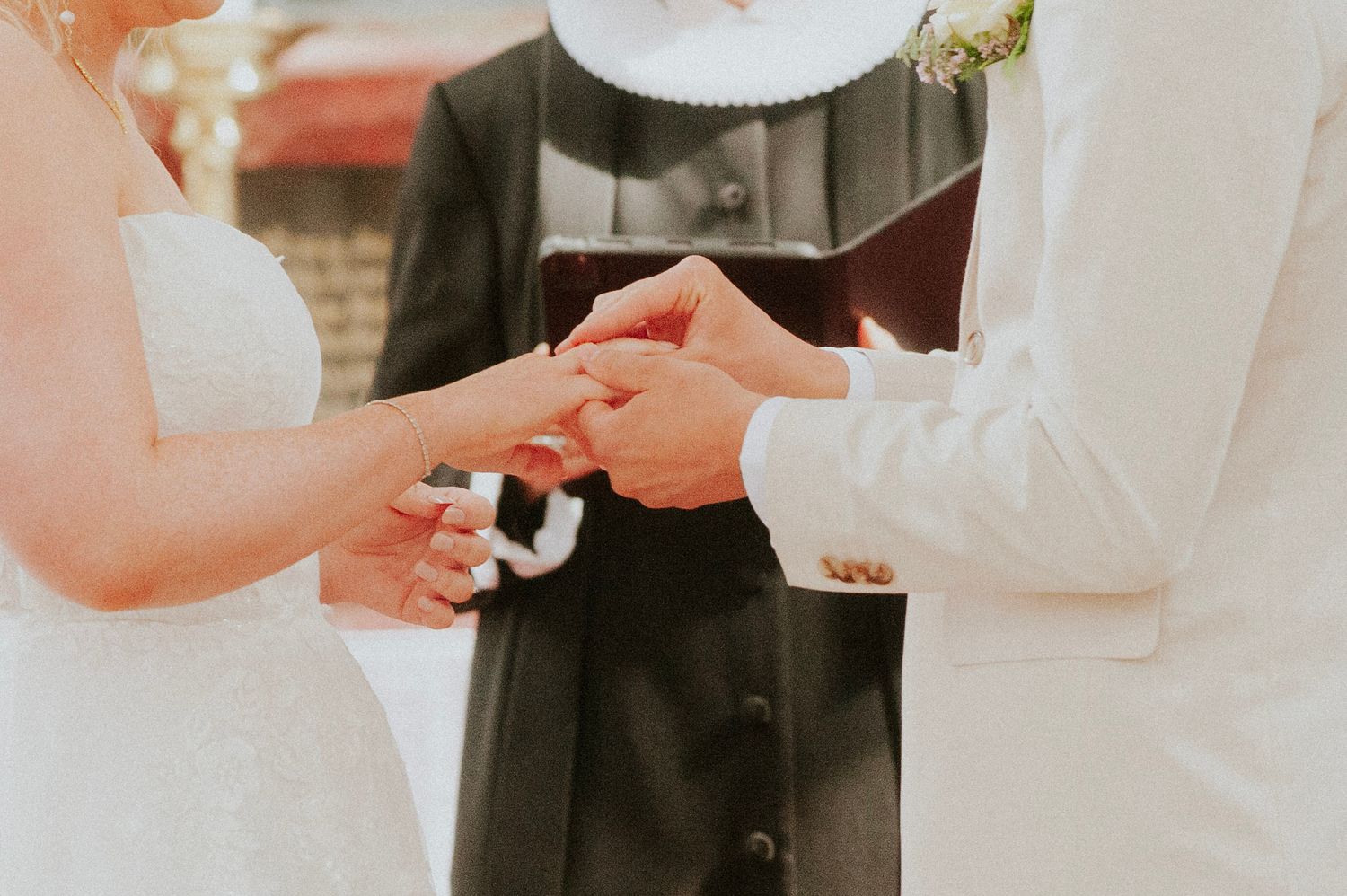Close-up of hands exchanging wedding rings during ceremony.