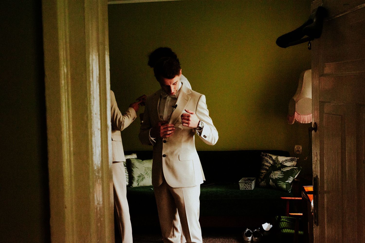 Someone in a light colored suit stands in a dimly lit room near a doorway.