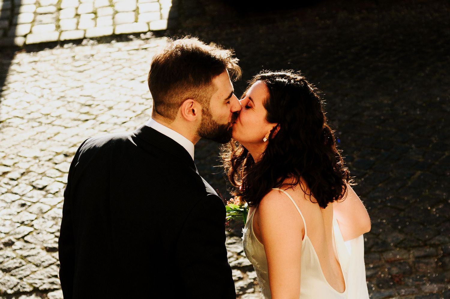 A romantic couple shares a tender kiss on a cobblestone street during their wedding photoshoot.