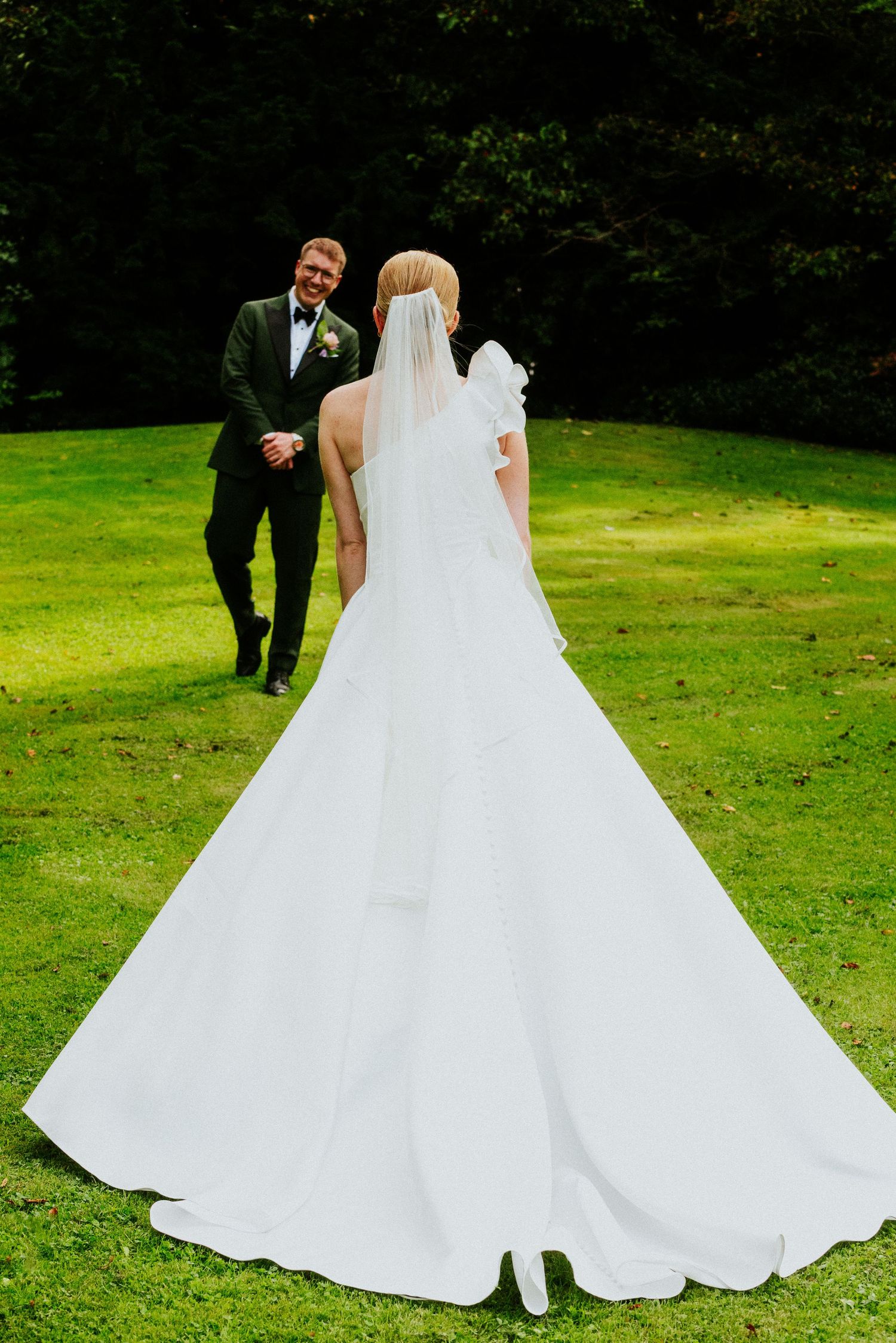 A flowing white wedding dress billows across a green lawn during outdoor photos.