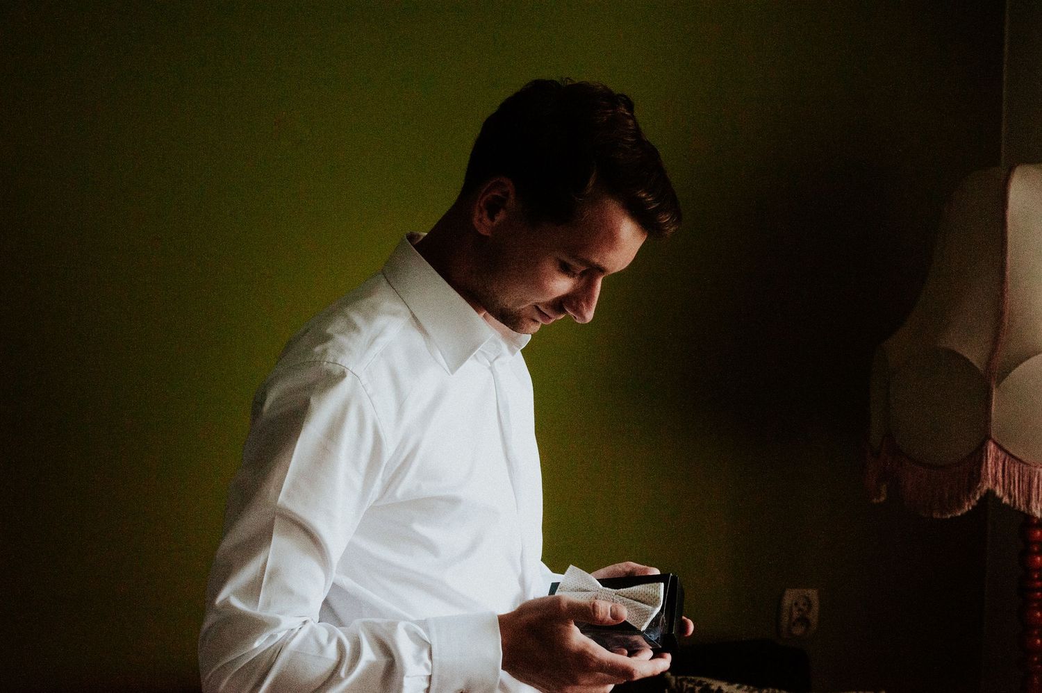 A person in a white button-down shirt looks down at a device in a dimly lit room with green walls.