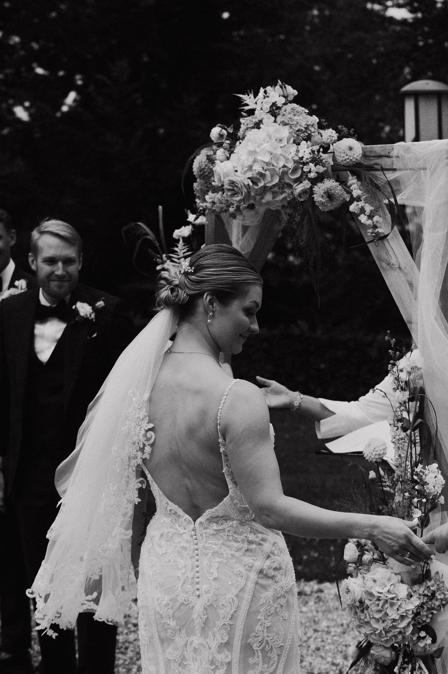 Black and white series of a bride in a lace gown with floral arrangements at an outdoor wedding setting.