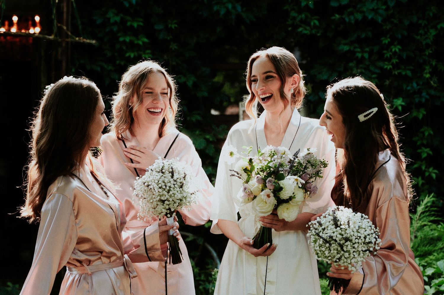 A group of people in light-colored dresses gather outdoors while holding delicate white baby's breath bouquets.