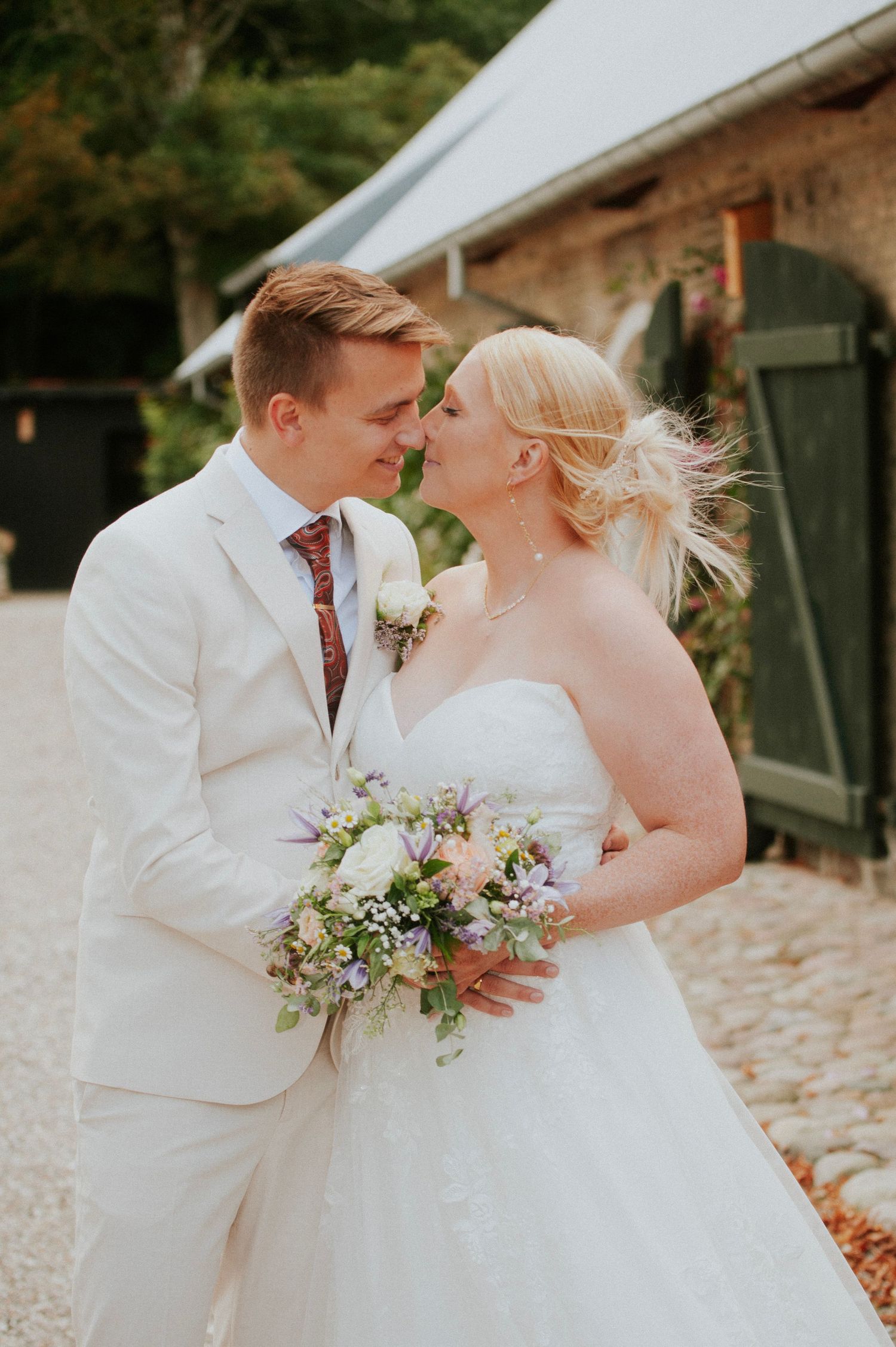Newlyweds share an intimate moment holding flowers outdoors.