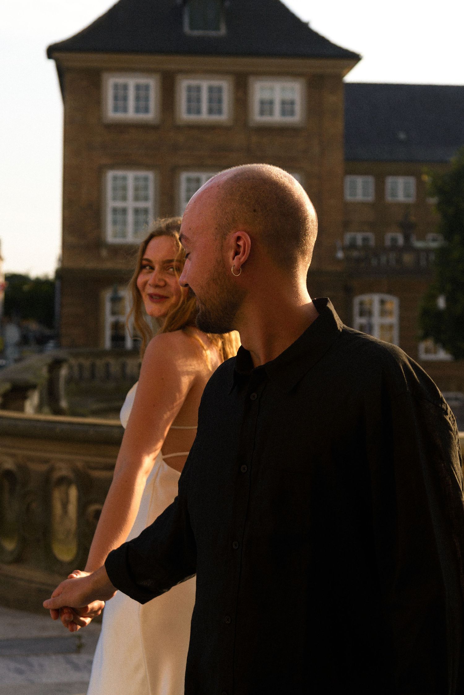A couple shares a tender moment at sunset in front of a traditional brick building.