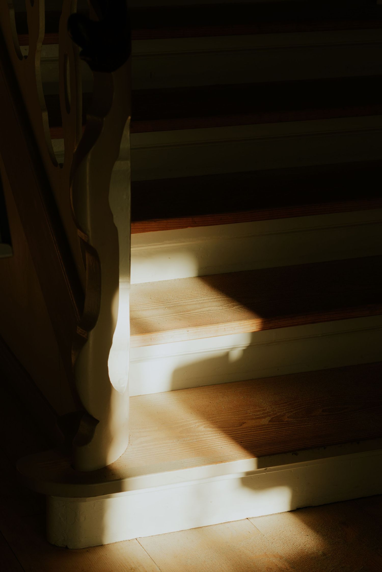 Sunlight streams through a window creating dramatic shadows on a wooden floor in a minimalist interior space.