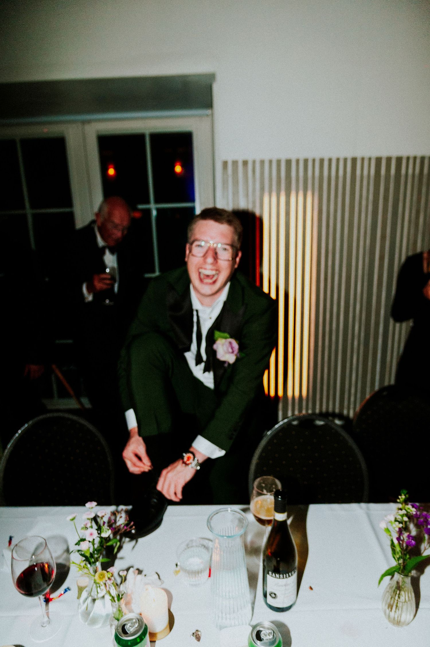 People seated at a long table with white tablecloths and floral centerpieces during a formal dinner event.