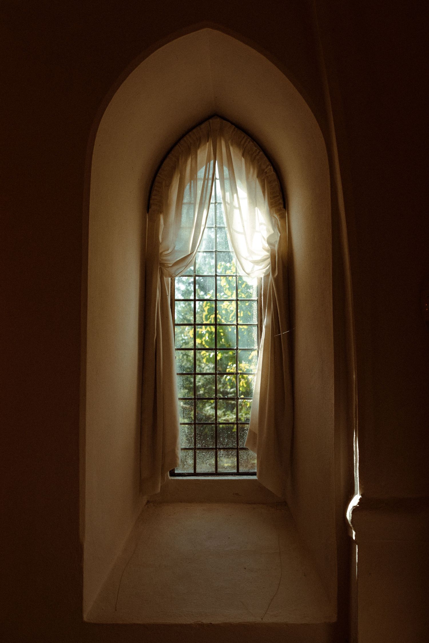 A sequence of arched windows with white curtains in a dimly lit hallway creating a dramatic architectural perspective.
