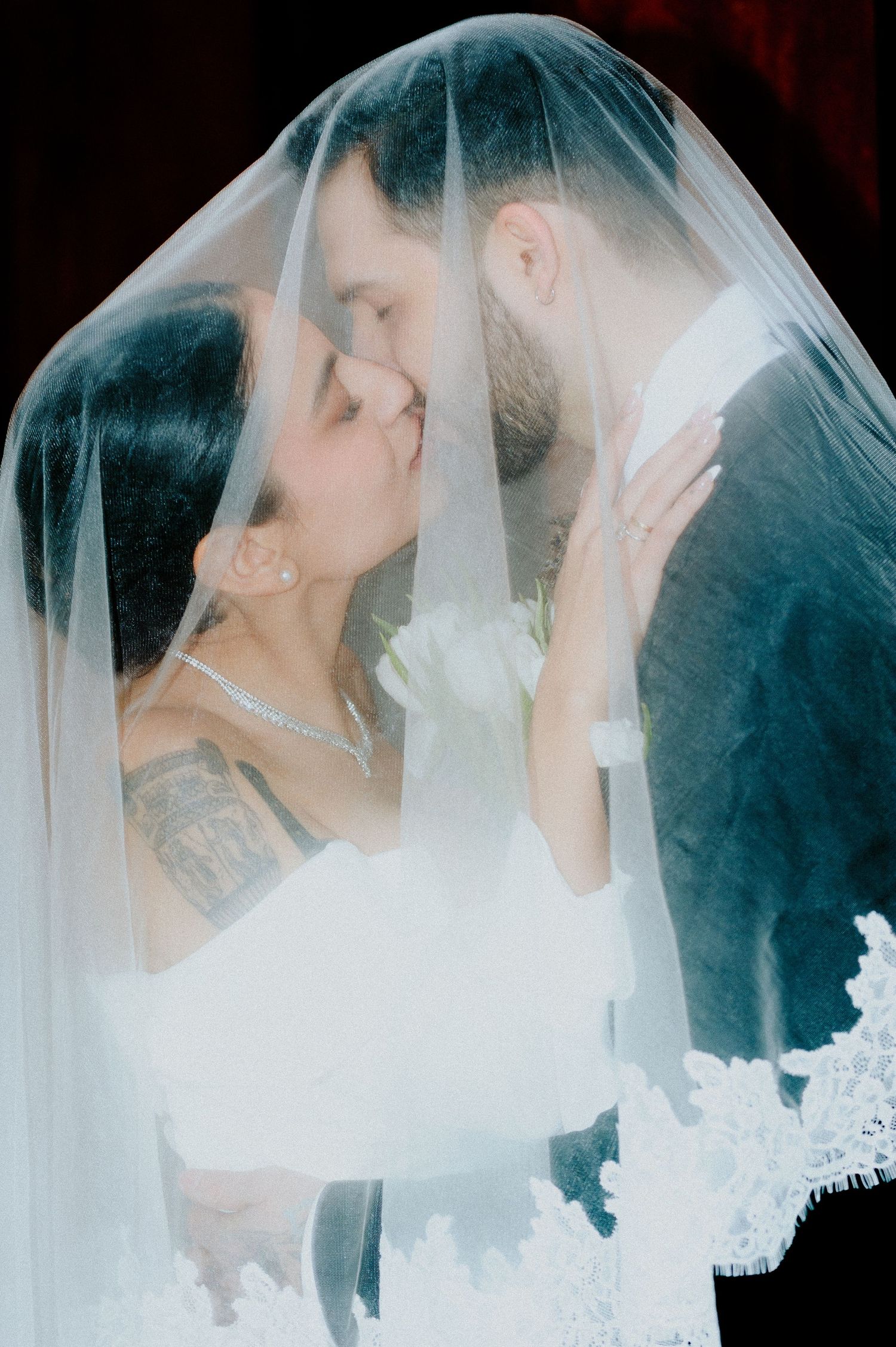 A romantic wedding moment captured under a delicate white veil as the couple shares their first kiss as newlyweds.