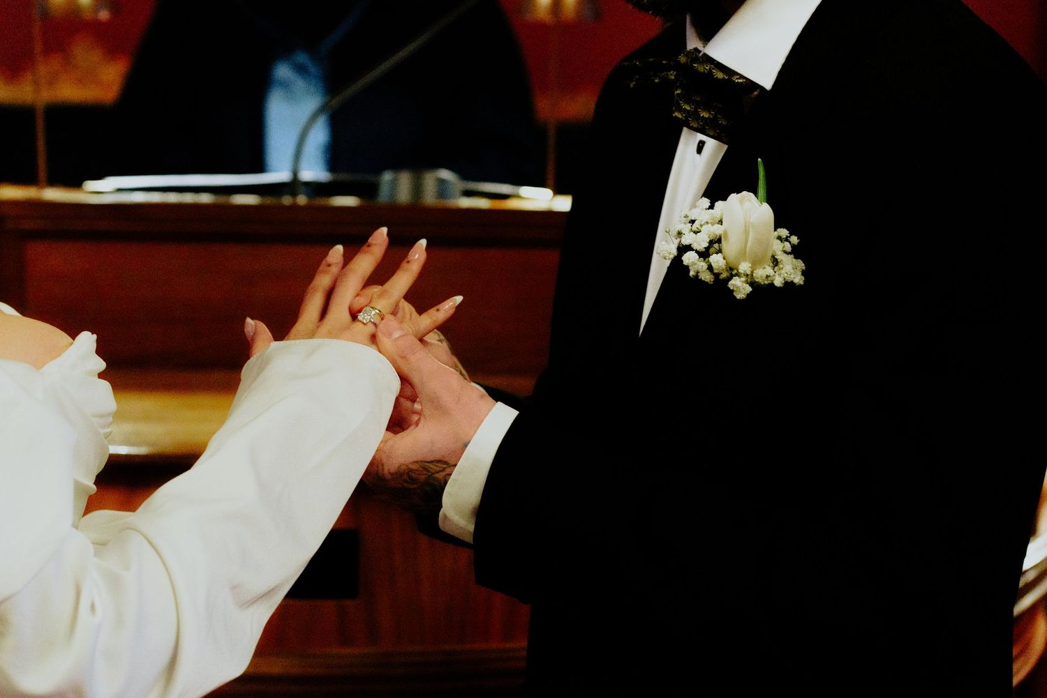 Close-up shot of hands exchanging rings during a wedding ceremony, with formal attire visible.