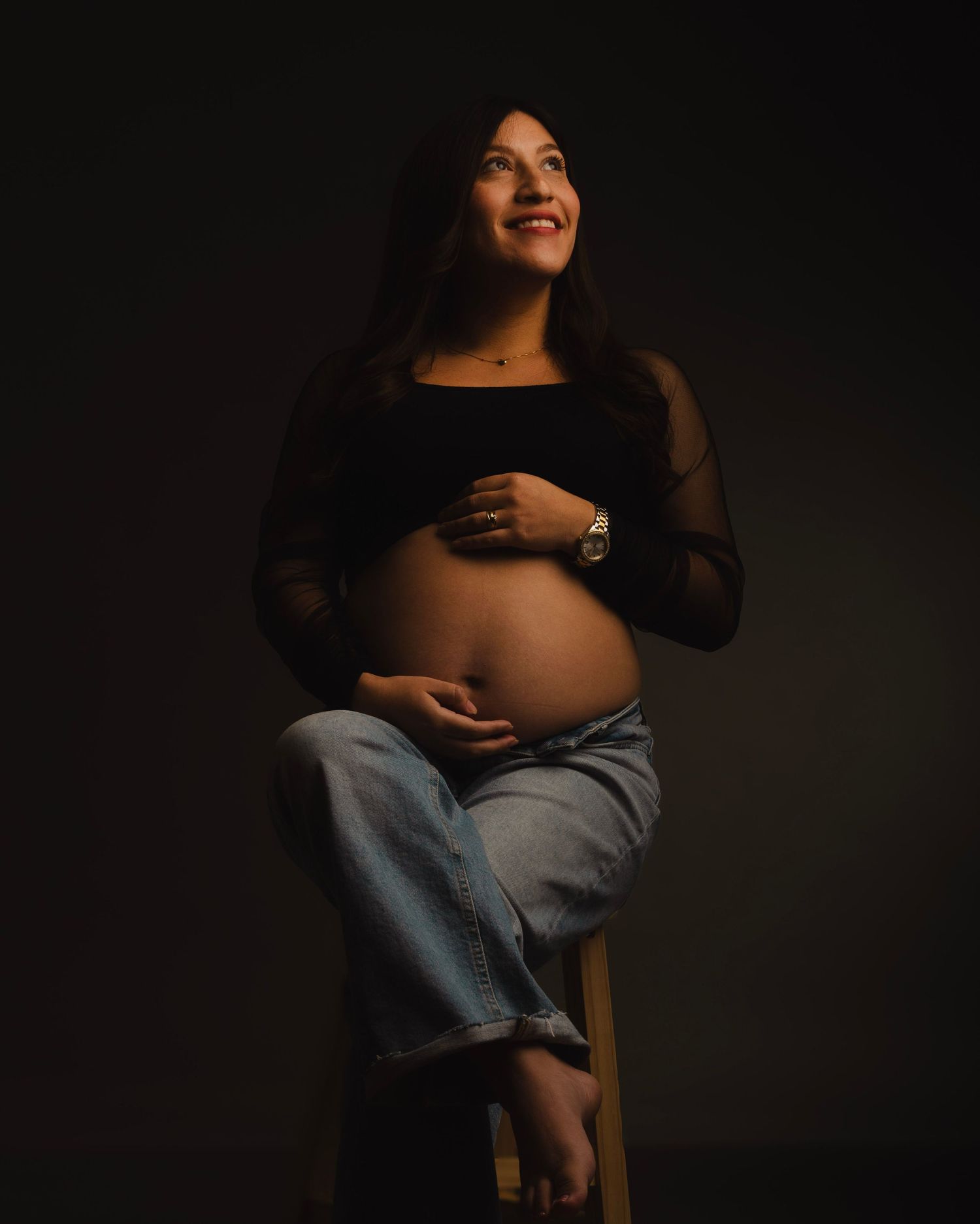 Silhouetted maternity portraits in dark moody lighting show a pregnant figure against a black background.