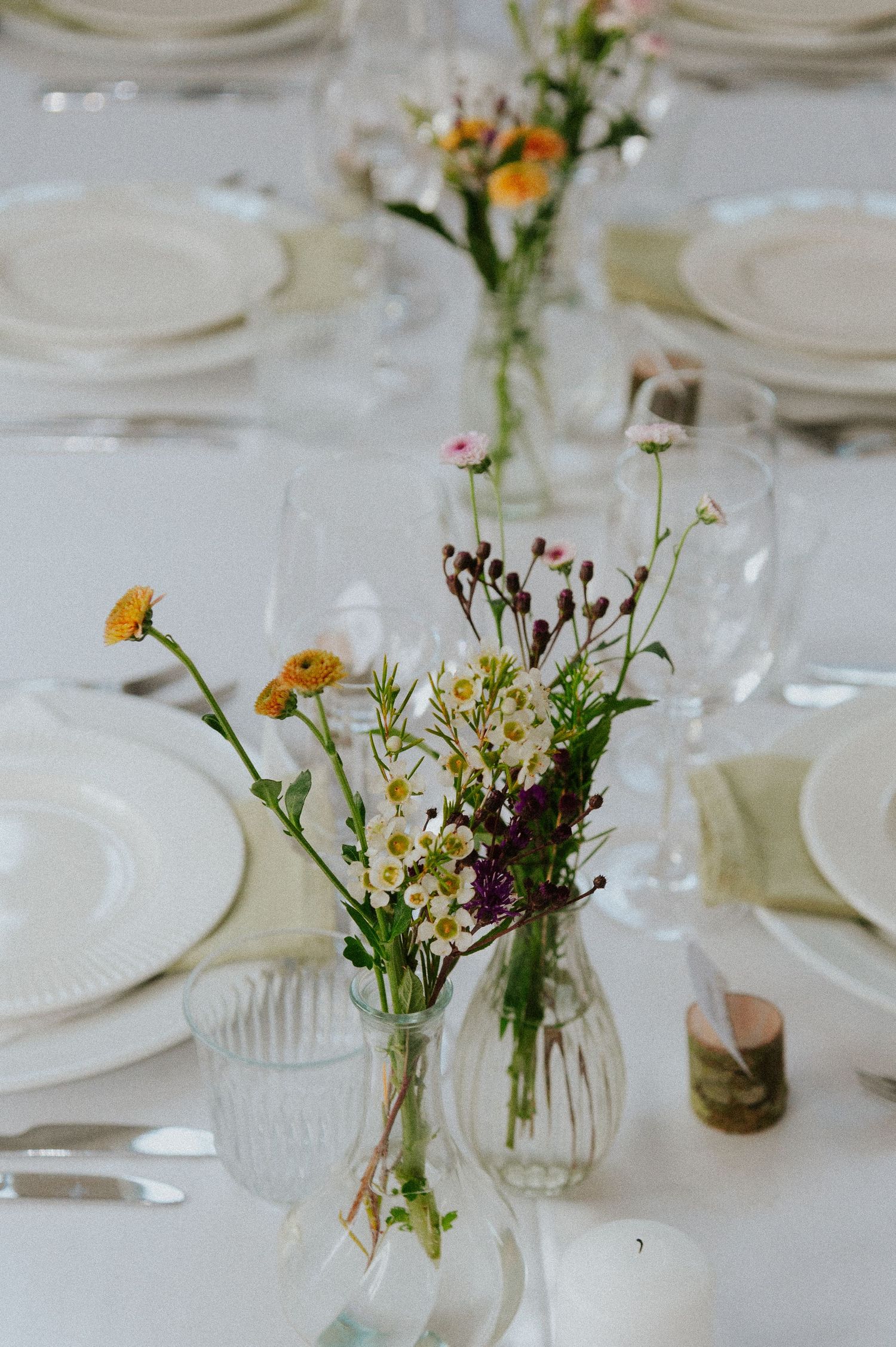Elegant wedding table setting with wildflowers in glass vases and white plates.