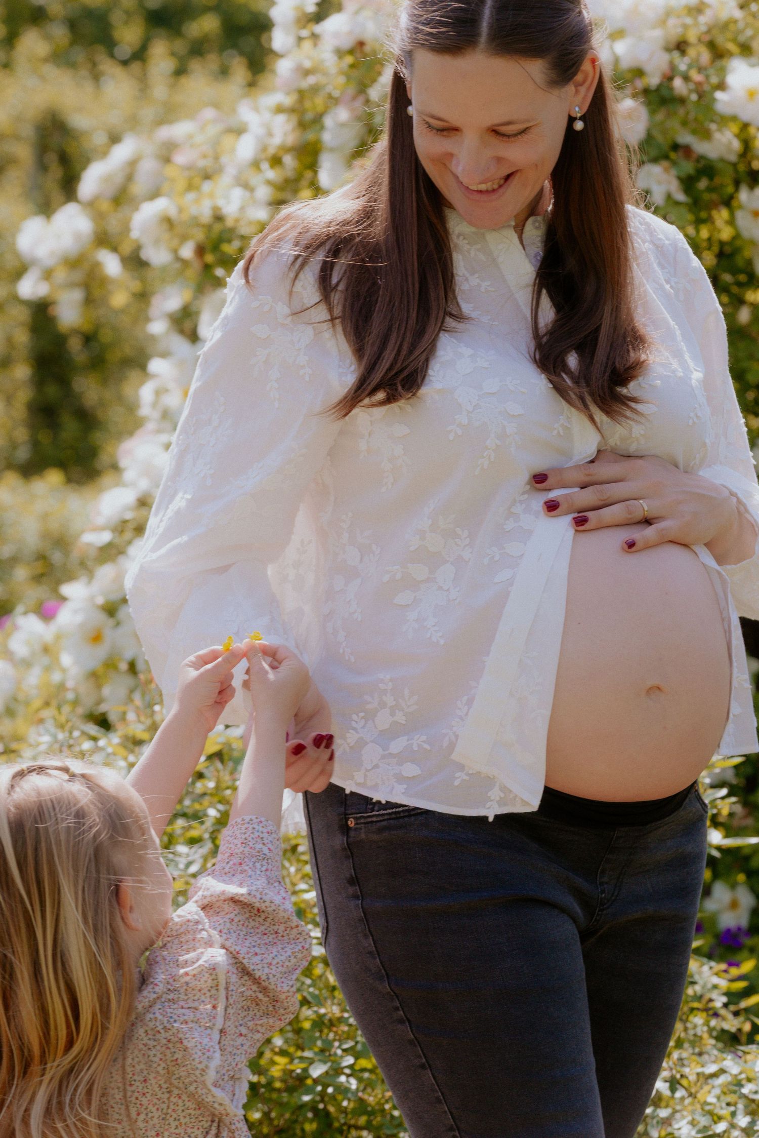 Mother and child share a tender moment in a garden setting with blooming flowers in the background.