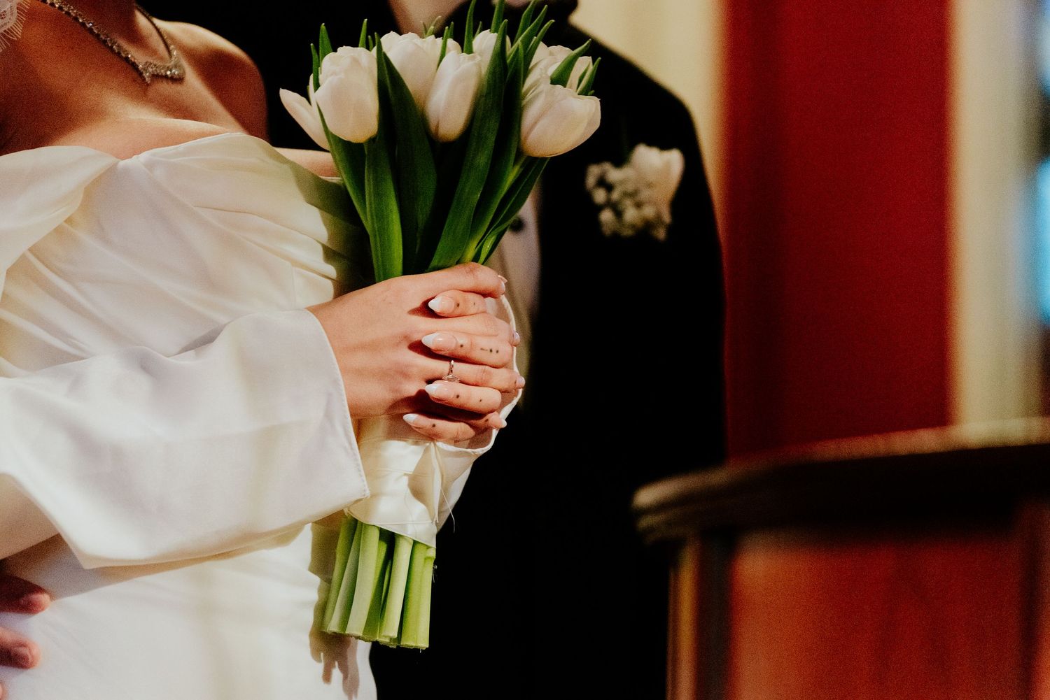 Close-up of white tulips held by bride in long-sleeved wedding dress.
