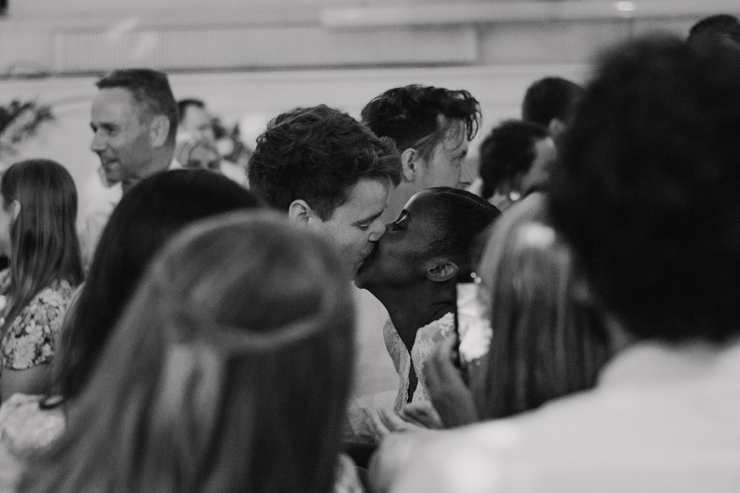 An intimate moment captured at a wedding reception with guests in the background.