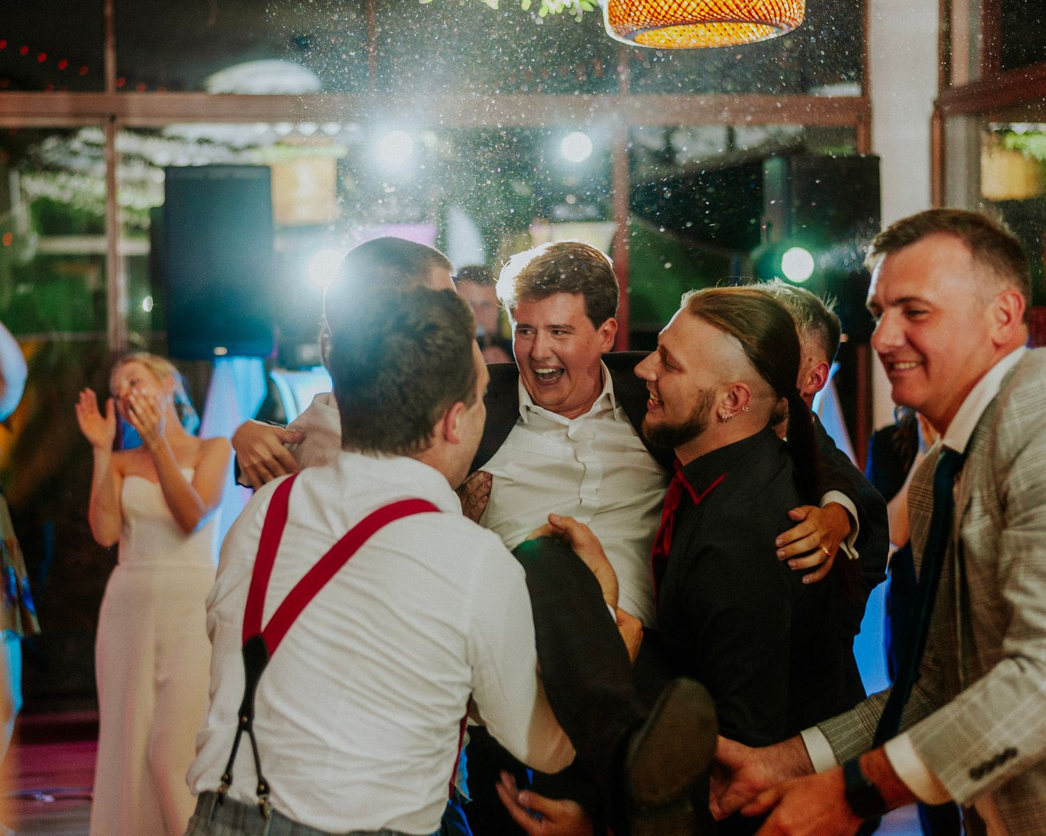 Energetic dance floor scene with wedding guests celebrating under colorful party lights.