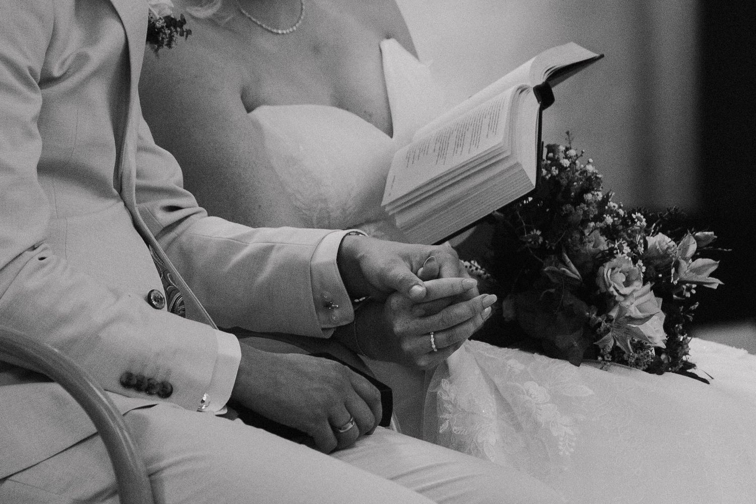 Close-up of wedding ceremony details with flowers and hands holding documents.