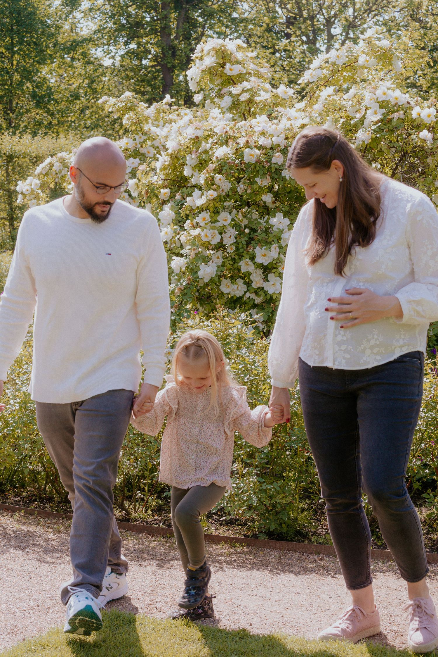 Parent and child play together outdoors on a sunny day surrounded by flowering bushes.