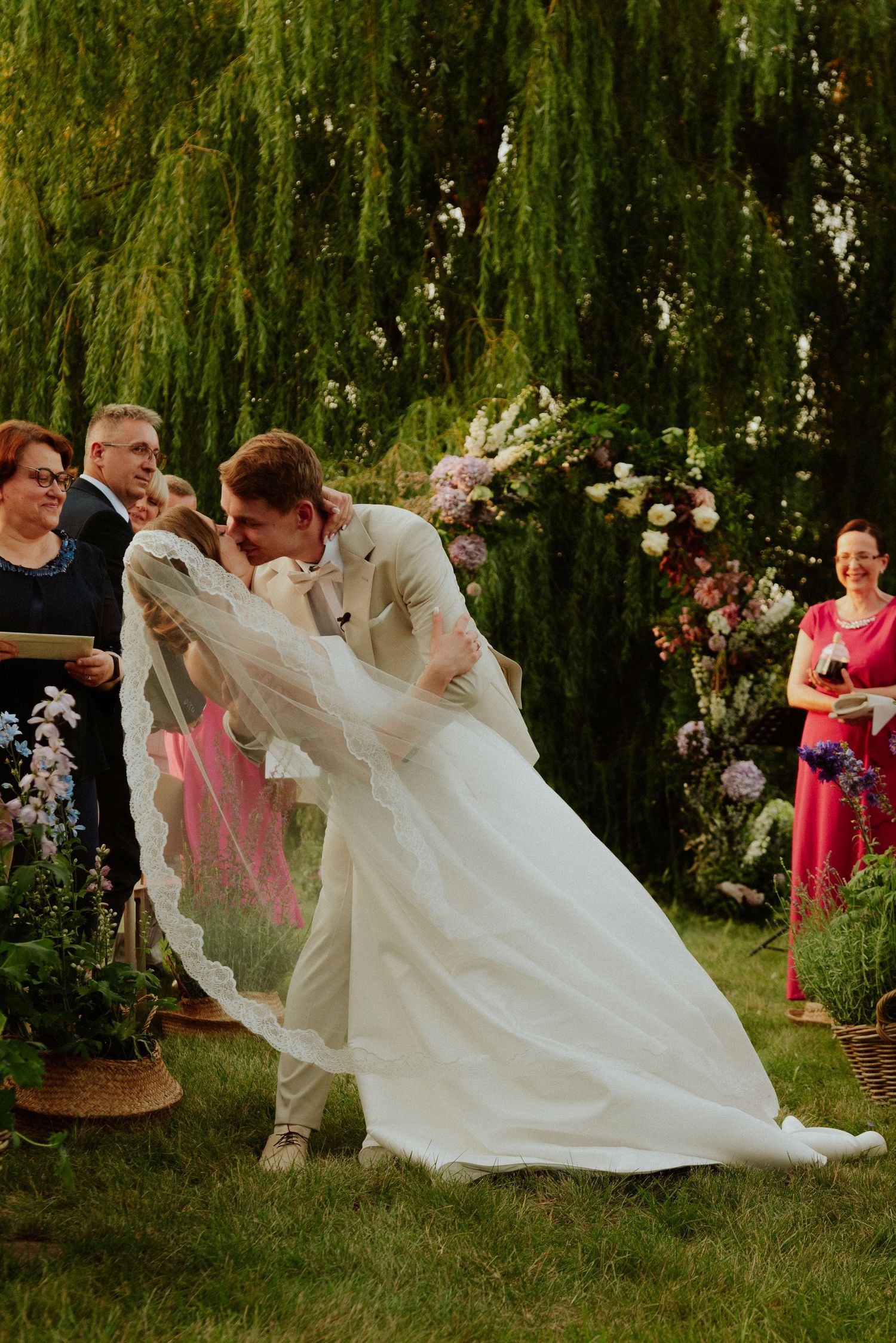 Sequence showing a playful wedding couple dipping and dancing under a weeping willow tree with guests watching.