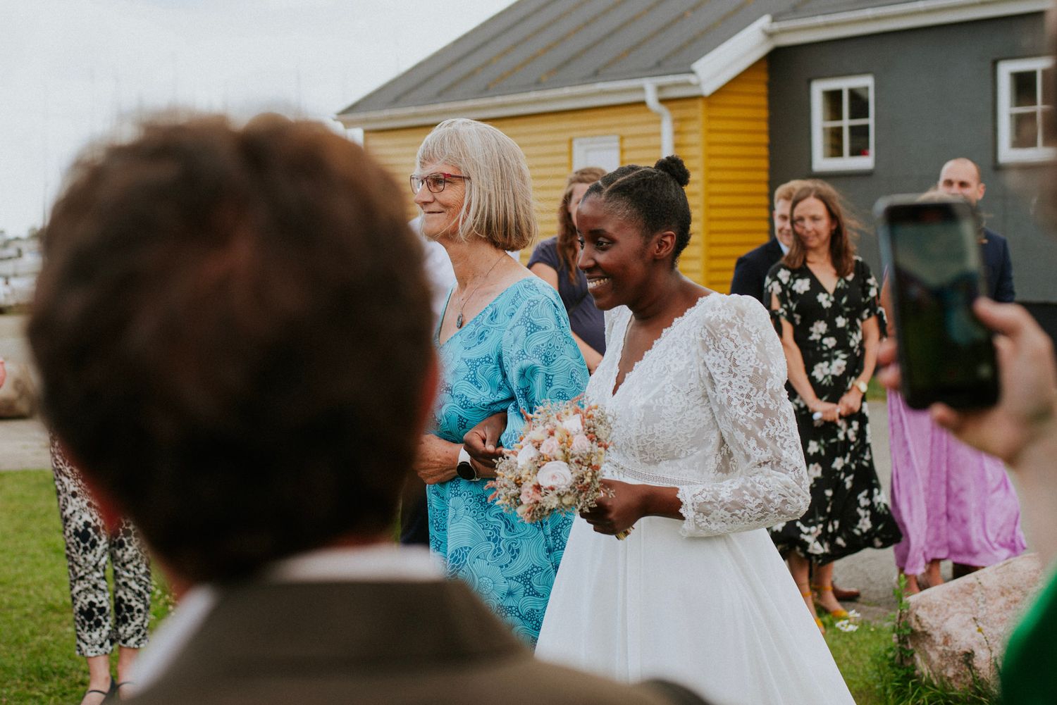 Wedding celebration outdoors with guests in floral dresses and colorful buildings in background.